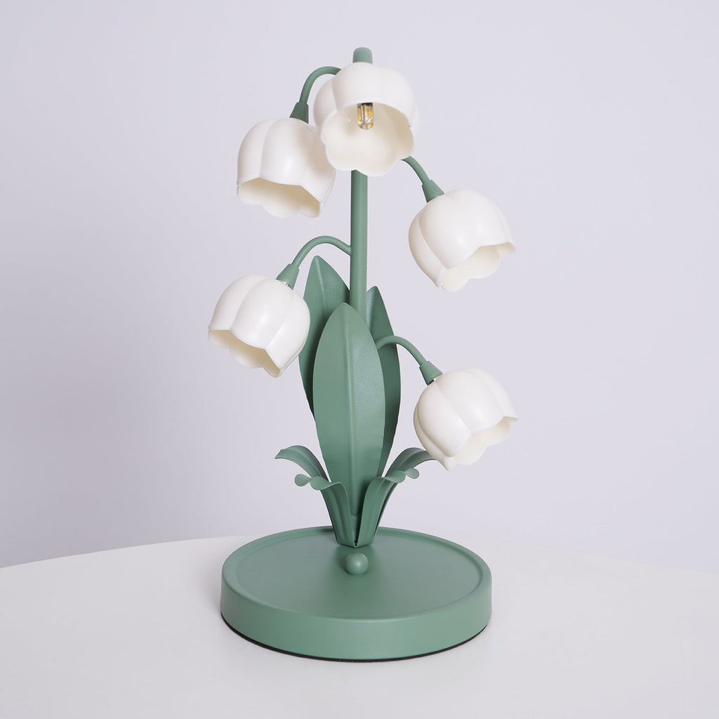 A Clérachic table lamp, switched off, with white bell shades on green stems and a round green base on a white table.