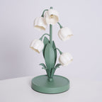 A Clérachic table lamp, switched off, with white bell shades on green stems and a round green base on a white table.