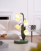A lit Clérachic table lamp on a white table near a cream sofa, with a black and white mug on a glass side table behind it.
