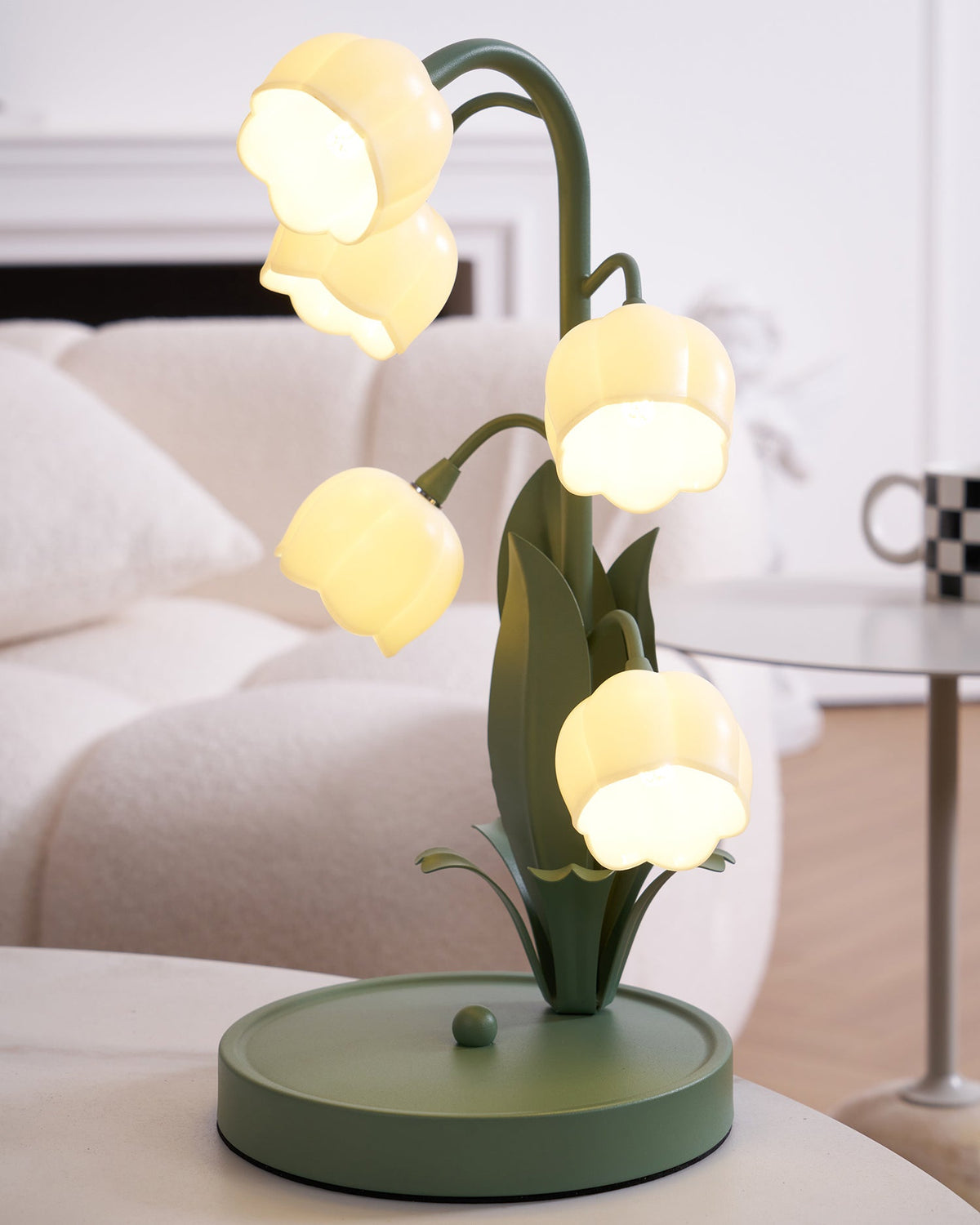 Clérachic table lamp lit in front of a white sofa and fireplace, with warm glowing bell shades on arched green stems.