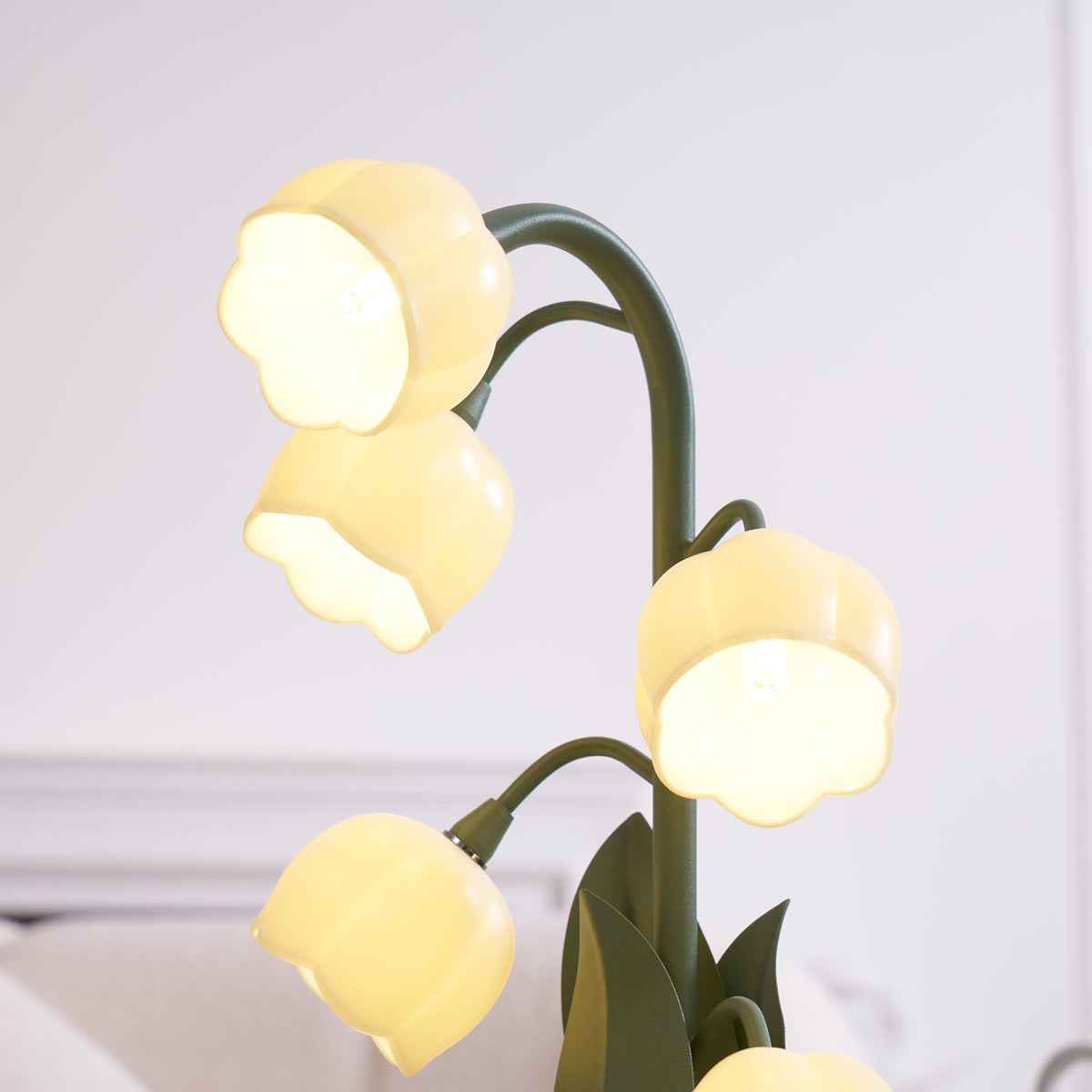Close view of the lit bell shades on this Clérachic table lamp, with cream furniture softly blurred behind it.