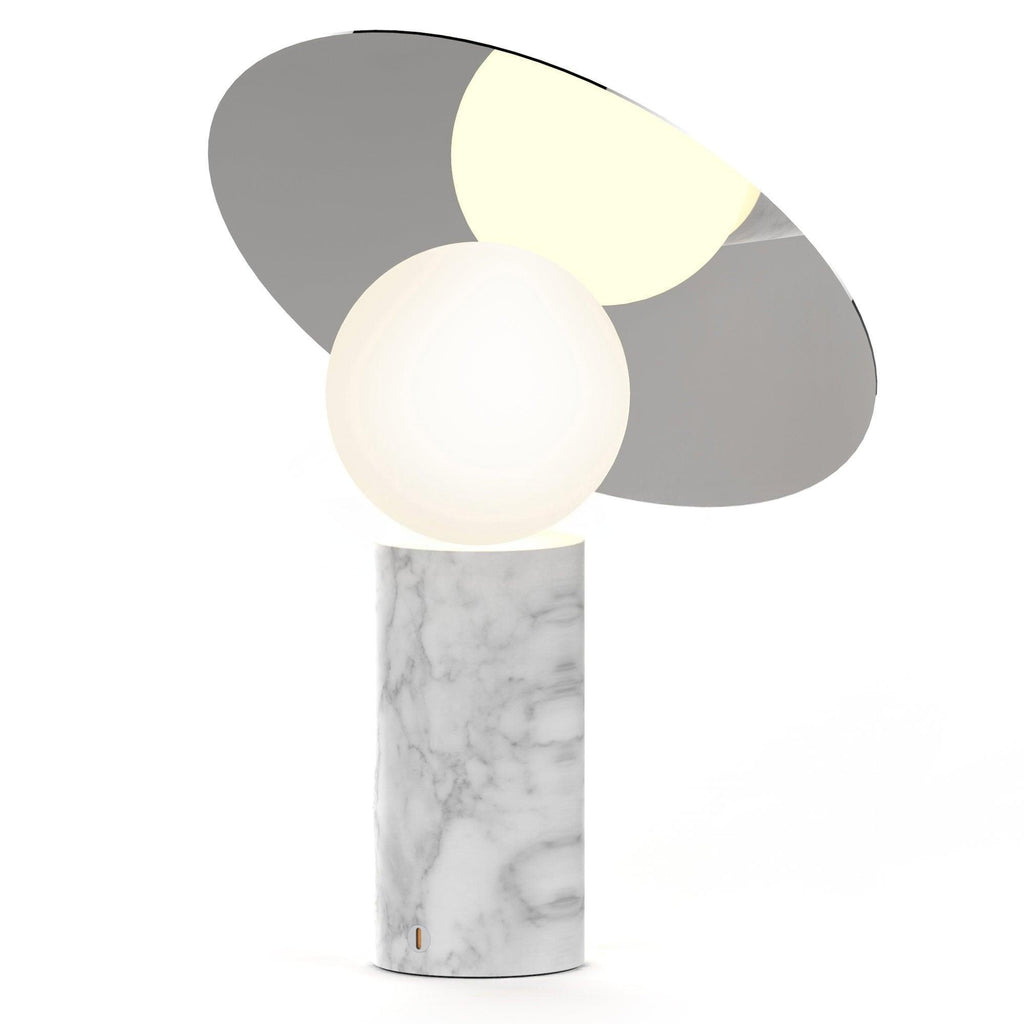 Clérachic tilting disc lamp lit on a plain white background, its white marble base paired with a grey and gold two-tone panel.