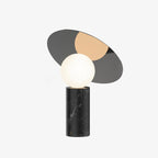 Clérachic tilting disc lamp on a plain white background, unlit, its grey and tan mirrored panel angled above a black marble base.