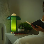 Clérachic green glass table lamp glowing on a white side table beside a stack of books and a small succulent pot.