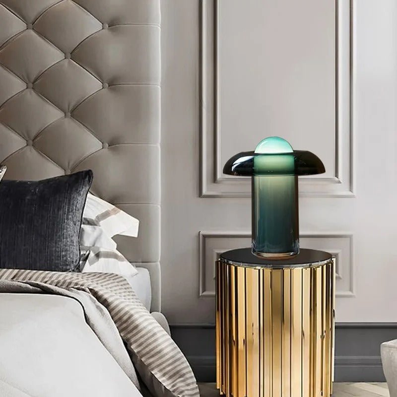 Clérachic green glass table lamp lit beside a tufted headboard, on a gold fluted drum bedside table.