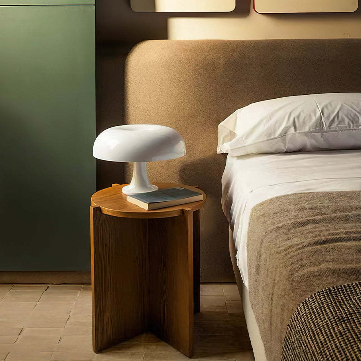 Small white dome lamp from Clérachic on a round wooden bedside table, next to a bed with grey bedding.