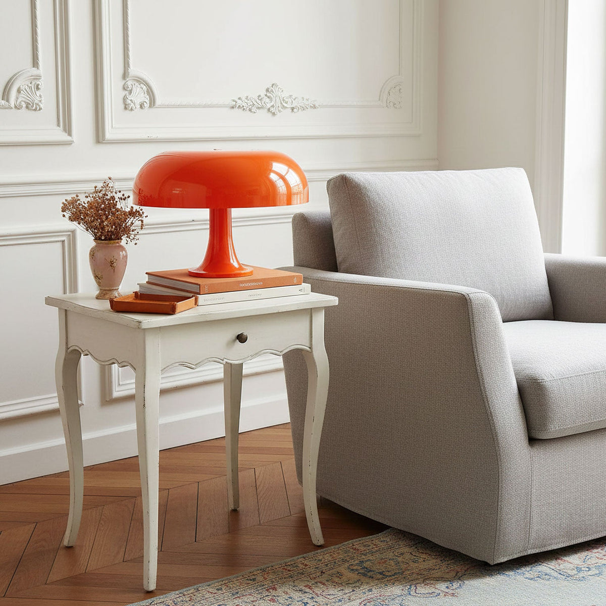 This Clérachic orange dome lamp on a white side table with a drawer, beside a grey armchair in a panelled room.