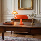 Orange mushroom lamp from Clérachic on a dark wood coffee table in a classic room with a gilt mirror and brass candelabra.