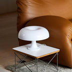 White dome table lamp from Clérachic on a low square side table with a wire frame, in front of a tan leather sofa.