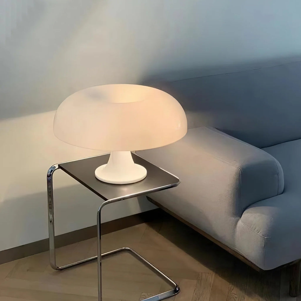 A white Clérachic dome lamp glowing softly on a chrome side table next to a pale blue-grey sofa.