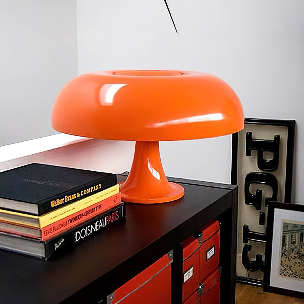 Close three-quarter view of the orange dome shade and stem on this Clérachic table lamp, set beside a stack of art books.