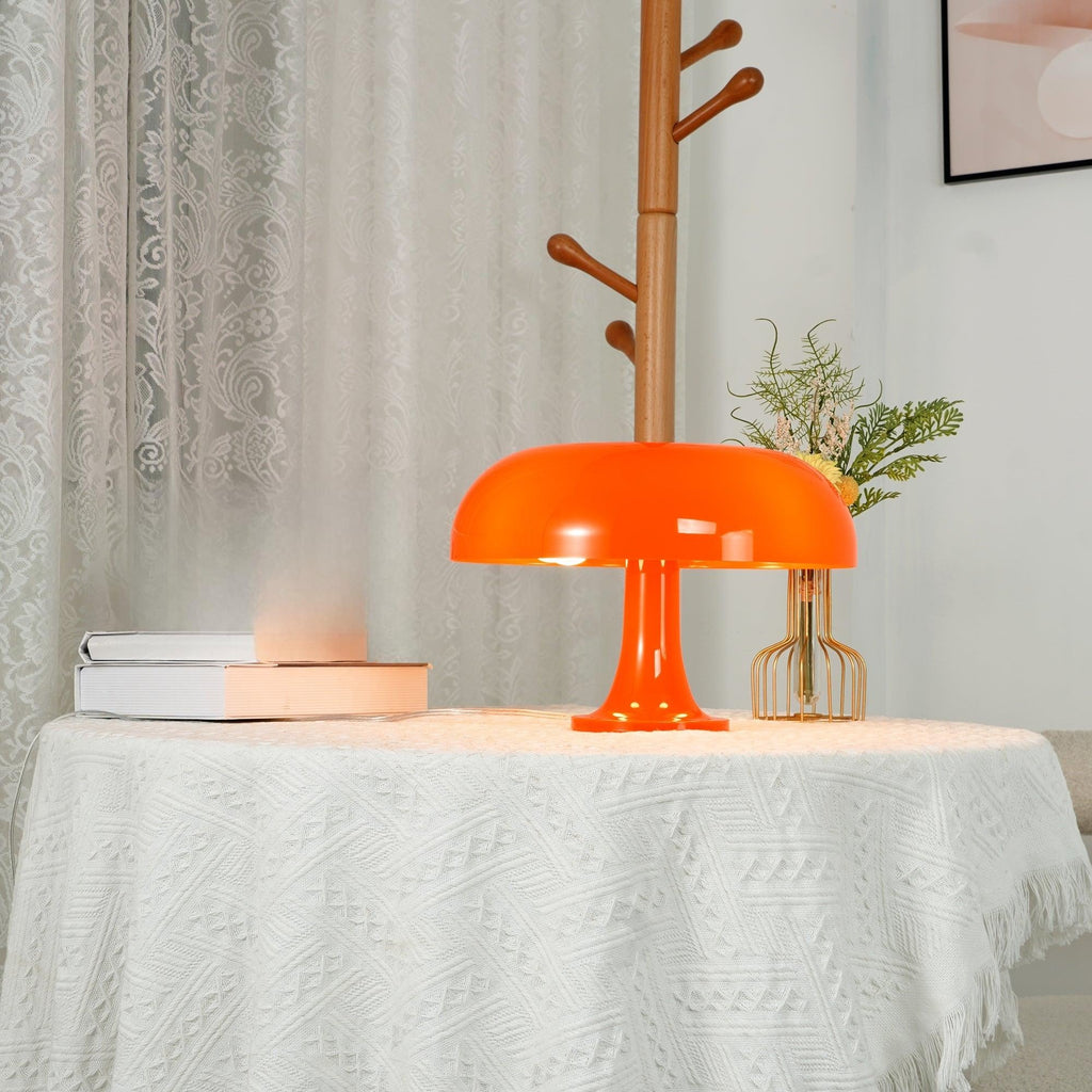 Orange Clérachic dome lamp lit on a white lace tablecloth, with a vase of flowers and books behind it.