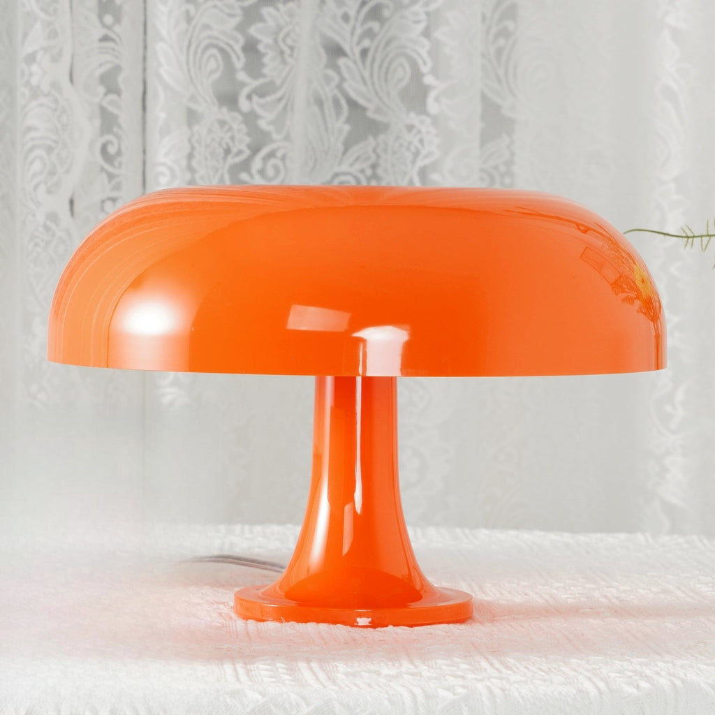 Low close view of the wide orange shade and slim stem of this Clérachic lamp, standing on a white lace cloth.
