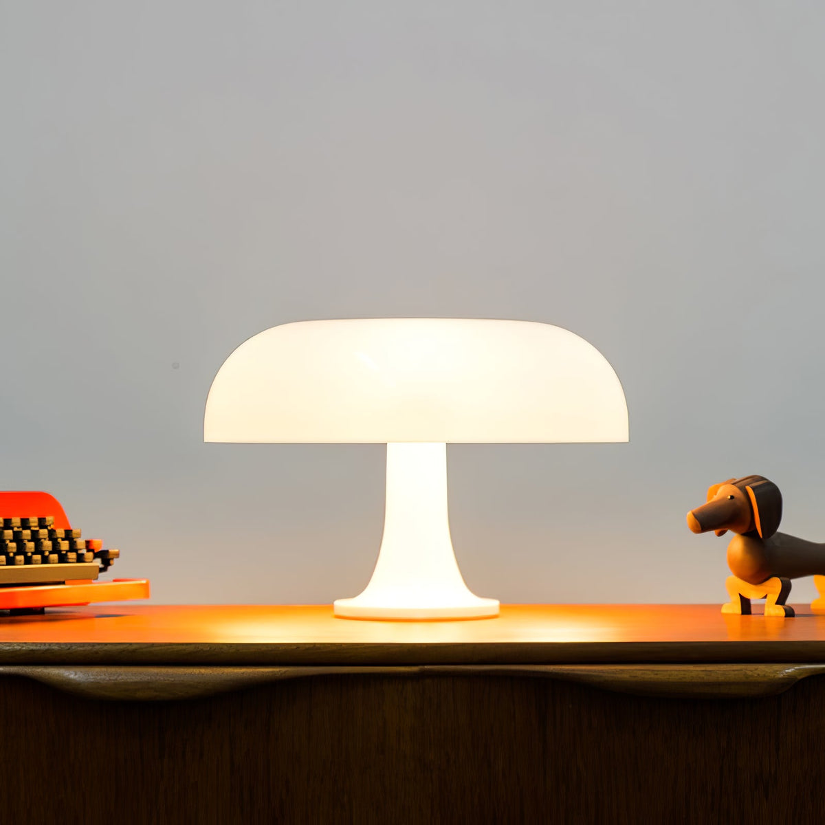 White dome table lamp from Clérachic lit on a dark wood sideboard, with a small dachshund figure to one side.