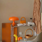 Orange Clérachic mushroom lamp on a chrome drinks trolley in a room with orange accessories and a tan wall.