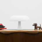 This Clérachic white mushroom lamp on a wooden sideboard against a pale wall, with a dachshund figure at the right.