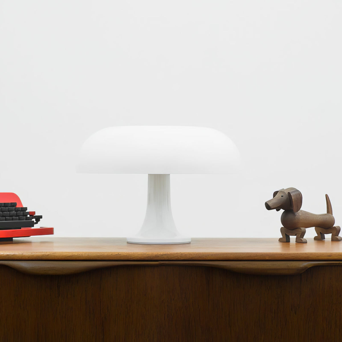 This Clérachic white mushroom lamp on a wooden sideboard against a pale wall, with a dachshund figure at the right.
