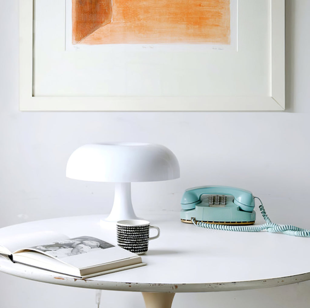White Clérachic table lamp on a round white table beside a teal telephone, a patterned mug and an open book.