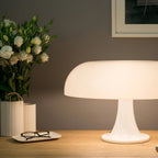 White Clérachic dome lamp on a pale wooden desk, with glasses on a small dish and white flowers beside it.