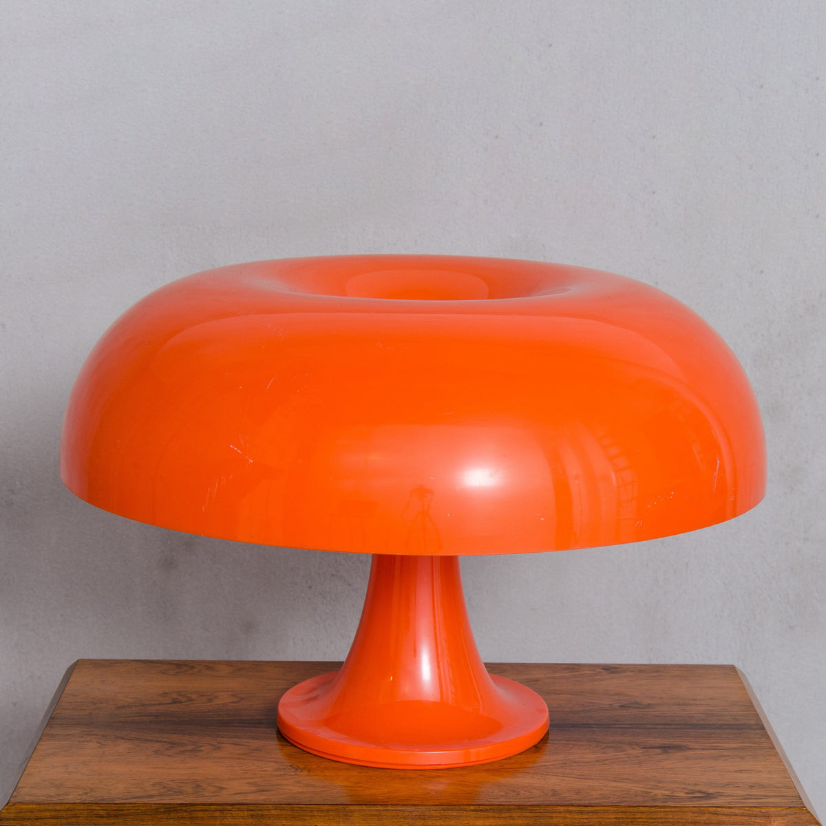 Large orange Clérachic table lamp on a wooden surface against a plain grey wall, its shade seen head on.