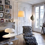 A Clérachic white dome lamp on a small marble side table in a bright room with tall windows and a lounge chair.