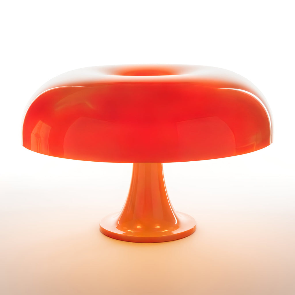 Orange Clérachic table lamp lit so the dome shade glows deep red-orange, on a white background with a warm halo below.