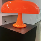 This Clérachic orange mushroom lamp on a black plinth in a pale room, the shade filling the top of the frame.