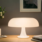 Close view of this Clérachic white dome lamp on a wooden desk, its shade glowing softly with glasses and books at the side.