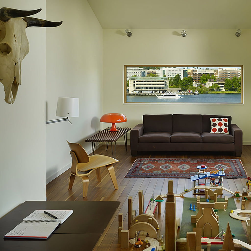 Small orange Clérachic lamp on a low table in a bright, open living room with a dark sofa and rug.