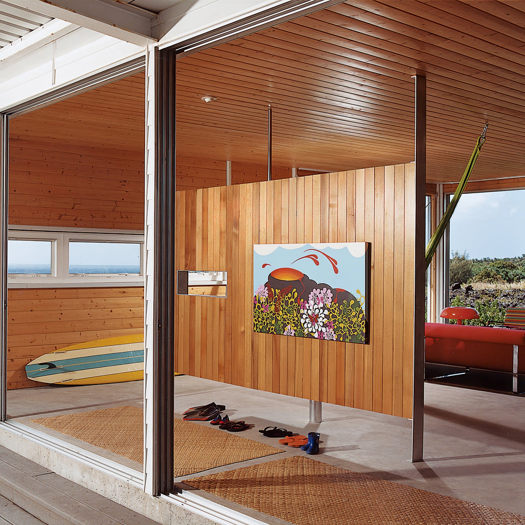 A Clérachic orange mushroom lamp seen from far across a wood-lined room with big glass doors and a surfboard on the wall.