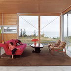 Orange Clérachic dome lamp on a low table in a wood-lined room with a view of the sea and a pink sofa.