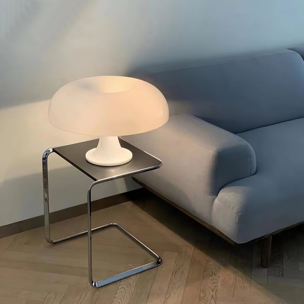 A Clérachic white dome lamp on a chrome side table, softly lit, next to a pale blue-grey sofa on a wood floor.