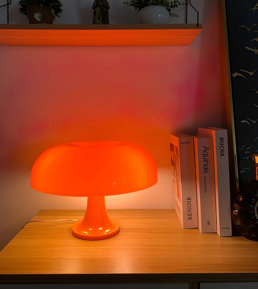 Orange Clérachic lamp glowing on a pine shelf beside books, its warm light spilling onto a pink-lit wall behind.