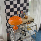 This Clérachic orange table lamp on a glass drinks trolley, with glassware, a record player and a checked wall behind.
