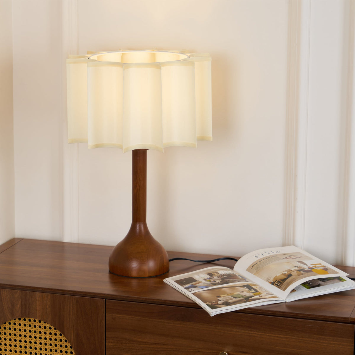 Lit Clérachic table lamp on a wooden sideboard, its pleated beige shade glowing above an open magazine.