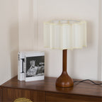 Straight-on view of a Clérachic table lamp with a tall scalloped shade, a book and black cord beside it.
