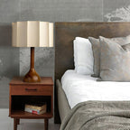 Clérachic table lamp on a mid-century bedside table, with white bedding and a grey throw beyond.