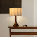 Lit Clérachic table lamp on a wooden console, its warm glow through the pleated shade and a dark artwork behind.