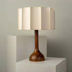 Unlit Clérachic table lamp on stacked pale plinths, the shade's flat panels and the teardrop-shaped wooden base clear.
