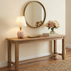 A small Clérachic table lamp with a pink marble base glows on a rustic wood console, under a round brass-framed mirror.