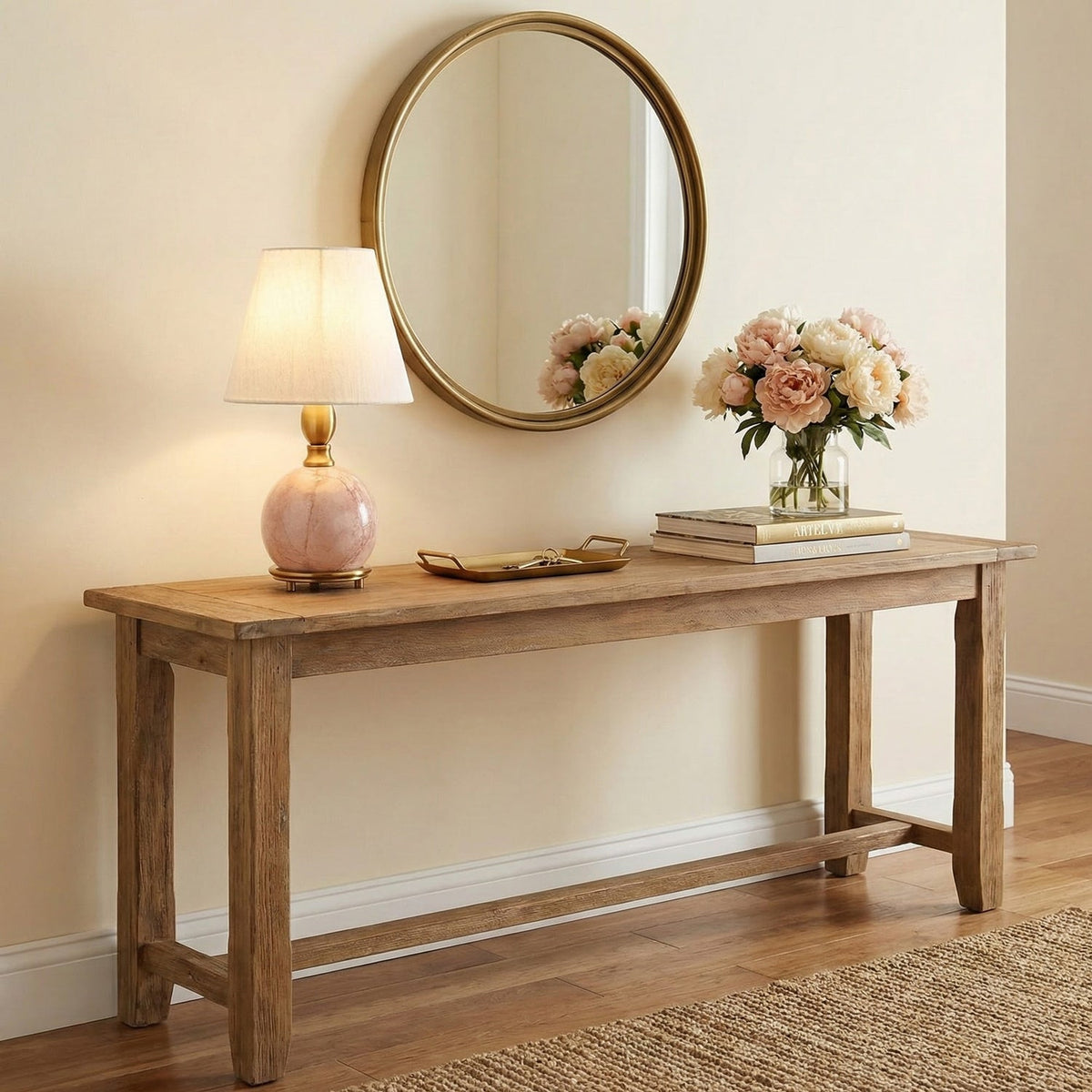 A small Clérachic table lamp with a pink marble base glows on a rustic wood console, under a round brass-framed mirror.