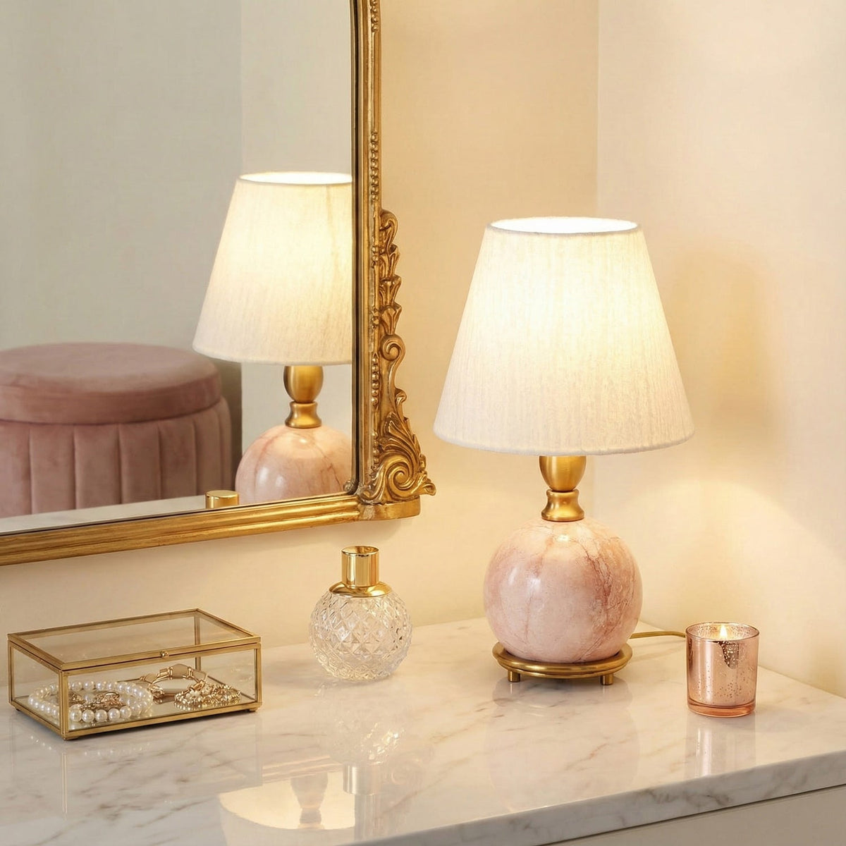 A Clérachic pink marble lamp on a white marble top, with a gilt mirror, a perfume bottle and a copper candle beside it.
