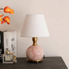A Clérachic table lamp on a dark shelf beside books and a perfume bottle, with orange flowers at the edge of the frame.
