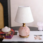 A Clérachic lamp with a pink marble base on a brass ring foot, sitting on a magazine beside a patterned box and a pink glass.