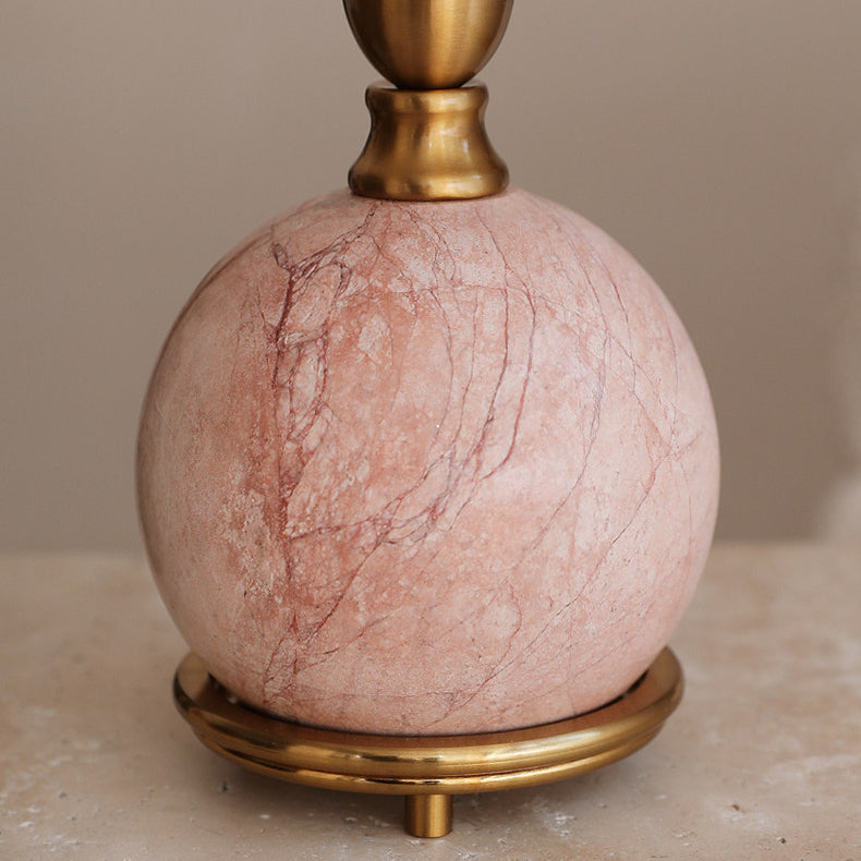 Close view of the pink marble ball base of this Clérachic lamp, showing its fine red veins, the brass collar and the ring foot.