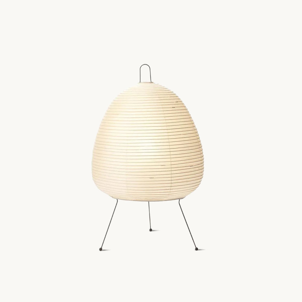 Pleated paper shade of this Clérachic table lamp on three slim black metal legs, shown on a plain white backdrop.