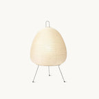 Pleated paper shade of this Clérachic table lamp on three slim black metal legs, shown on a plain white backdrop.