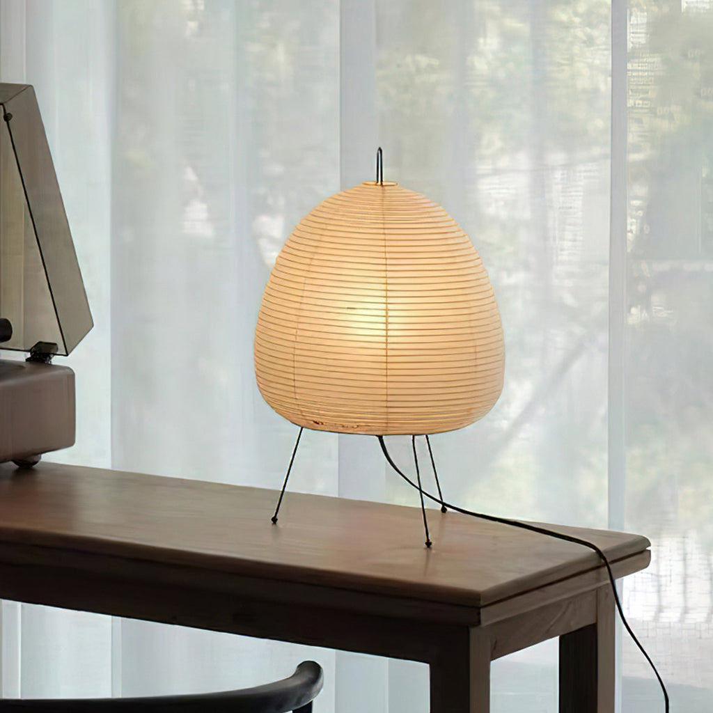 This Clérachic paper table lamp glowing softly on a dark wooden console beside sheer curtains, its black cord trailing down.