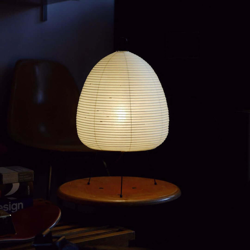 In a dark room, this Clérachic paper lamp glows as the only light, sitting on a round wooden stool.