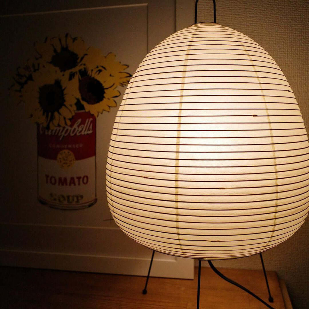 Close view of the ribbed paper shade on this Clérachic table lamp, glowing in front of a pop-art style poster.